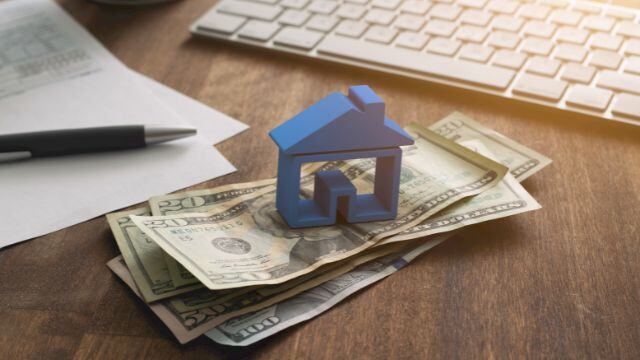 a blue home figurine resting on a money with a contract in the background