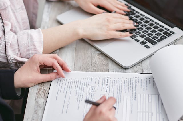 Person filling out a document next to a laptop